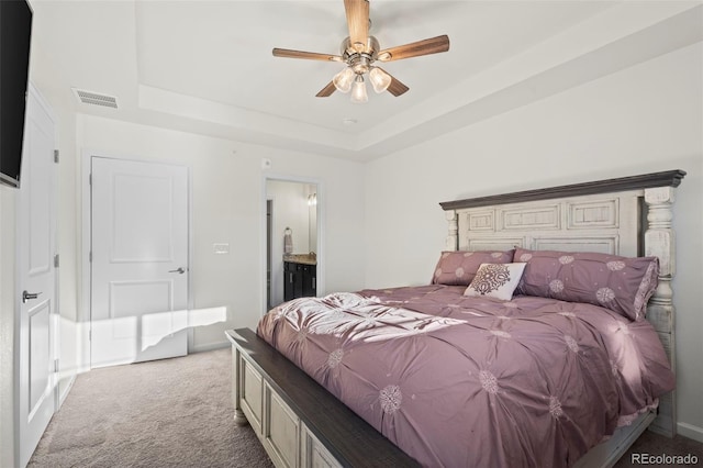 carpeted bedroom with ensuite bath, ceiling fan, and a tray ceiling