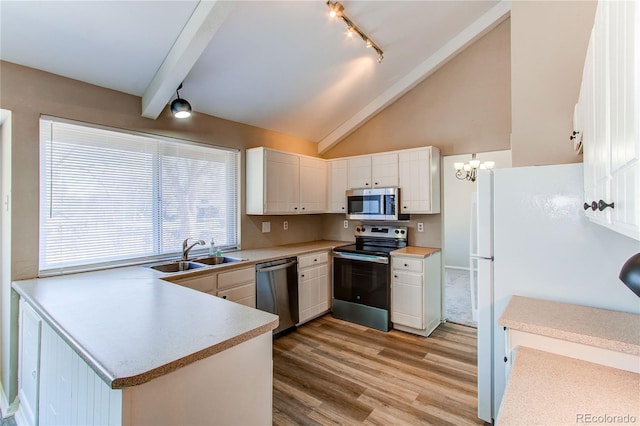 kitchen featuring stainless steel appliances, light countertops, light wood-style flooring, a sink, and a peninsula