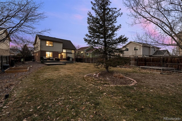 back of property at dusk featuring a yard, brick siding, and a fenced backyard