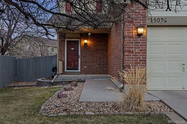 view of exterior entry with brick siding, an attached garage, and fence