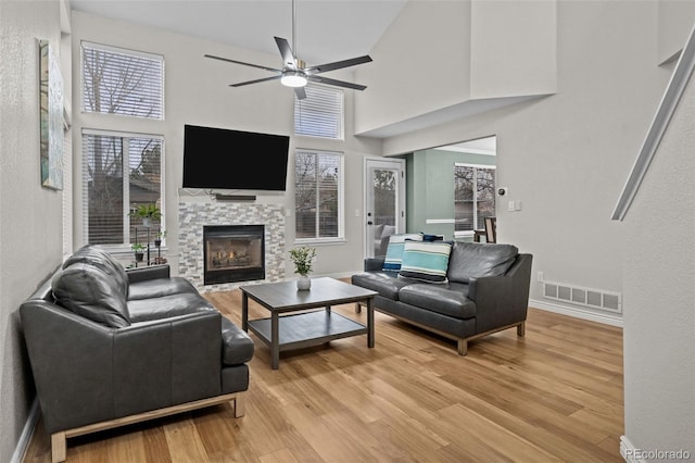 living area with light wood finished floors, a fireplace, visible vents, and a ceiling fan