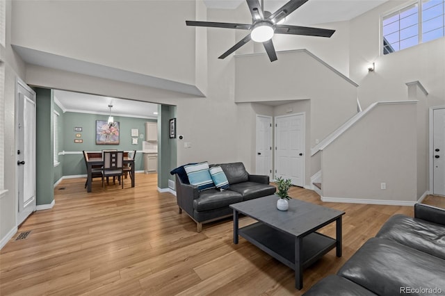 living area featuring baseboards, visible vents, a ceiling fan, stairway, and light wood-type flooring