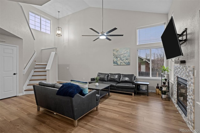 living room with high vaulted ceiling, stairway, a fireplace, and light wood-style floors