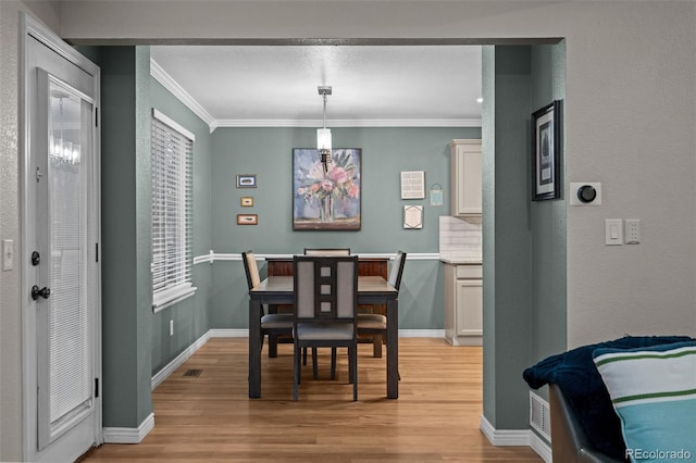 dining room with baseboards, crown molding, visible vents, and light wood finished floors