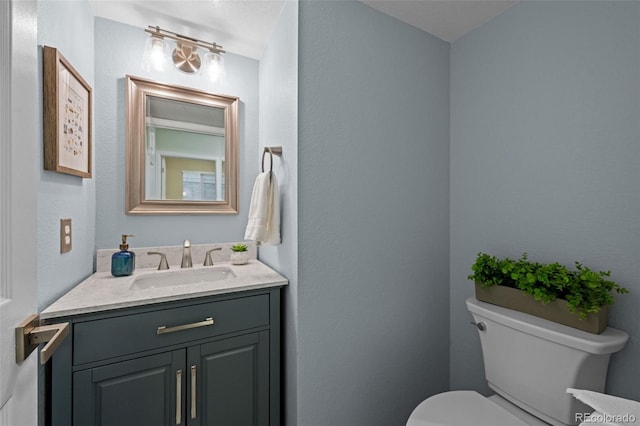 half bath featuring toilet, a textured wall, and vanity