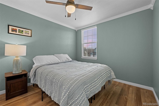 bedroom with a ceiling fan, crown molding, baseboards, and wood finished floors