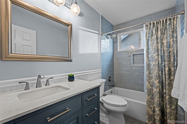 bathroom with a textured wall, toilet, a wainscoted wall, vanity, and shower / bath combination with curtain