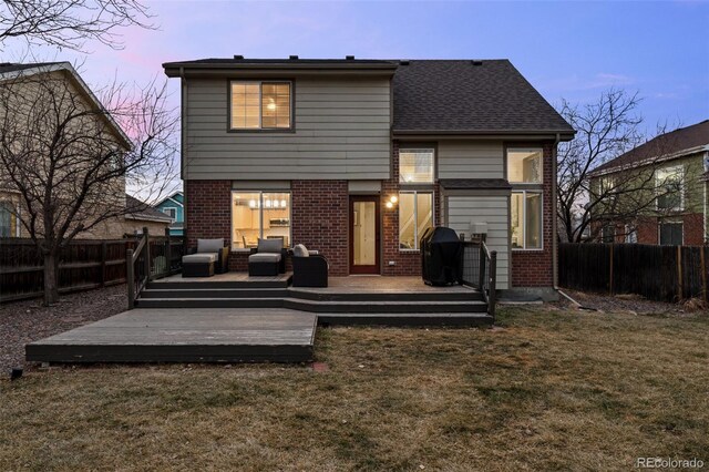 back of house at dusk featuring a yard, brick siding, a fenced backyard, and a wooden deck