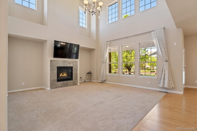 unfurnished living room featuring light wood-type flooring, a high ceiling, a tile fireplace, and a chandelier