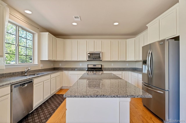 kitchen featuring white cabinets, a kitchen island, light stone countertops, and stainless steel appliances