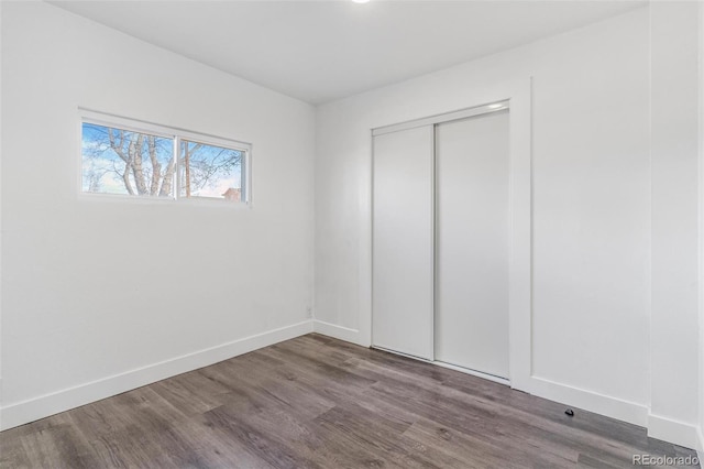 unfurnished bedroom featuring wood finished floors, baseboards, and a closet