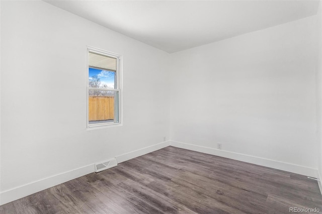 empty room featuring dark wood-style floors, visible vents, and baseboards