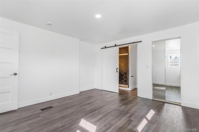 unfurnished bedroom featuring a barn door, baseboards, visible vents, and dark wood-style flooring