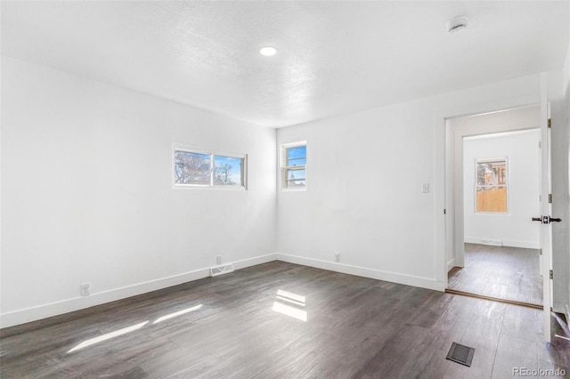 spare room with visible vents, baseboards, and dark wood-type flooring