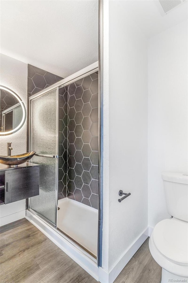 bathroom featuring wood finished floors, baseboards, visible vents, a stall shower, and toilet