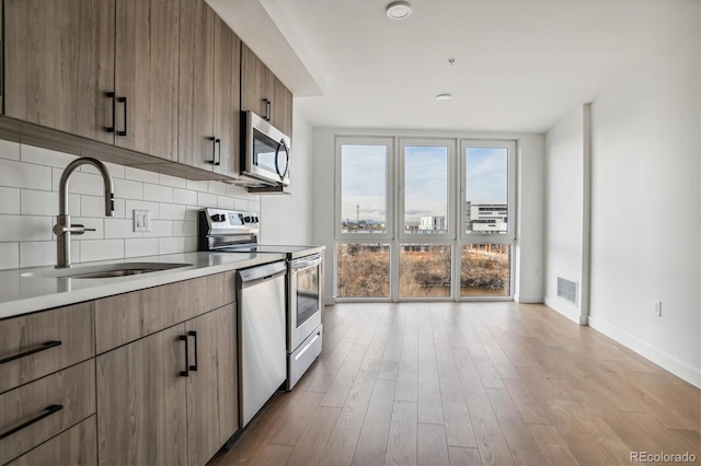 kitchen featuring floor to ceiling windows, sink, light wood-type flooring, tasteful backsplash, and stainless steel appliances