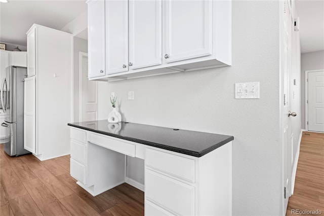 kitchen featuring white cabinets, built in desk, light hardwood / wood-style floors, and stainless steel refrigerator