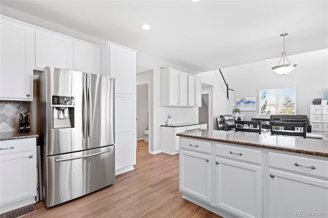 kitchen with decorative backsplash, stainless steel fridge, white cabinetry, and hanging light fixtures