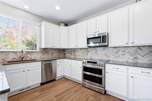 kitchen with dark stone countertops, white cabinetry, sink, and stainless steel appliances