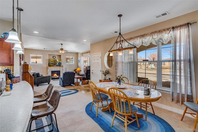 dining space featuring light colored carpet, a glass covered fireplace, visible vents, and baseboards