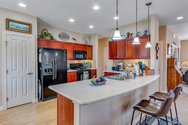 kitchen featuring a peninsula, black appliances, a kitchen bar, and light countertops