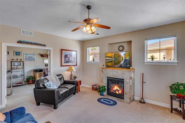 carpeted living room featuring baseboards, visible vents, ceiling fan, and a tiled fireplace