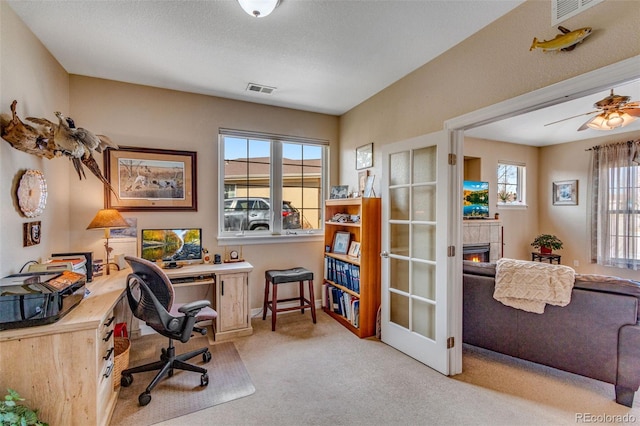 home office with visible vents, light colored carpet, a ceiling fan, and a tile fireplace