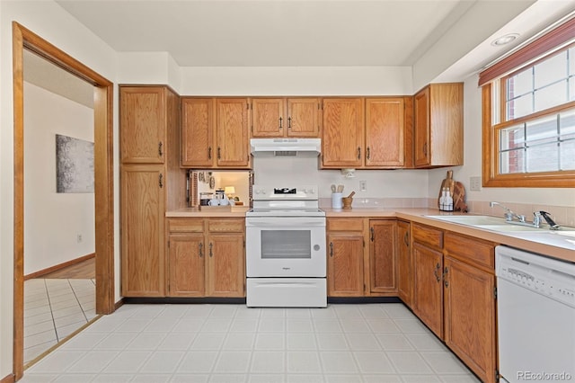 kitchen with white appliances, under cabinet range hood, light countertops, and a sink