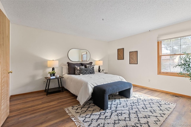 bedroom with baseboards, a textured ceiling, visible vents, and wood finished floors