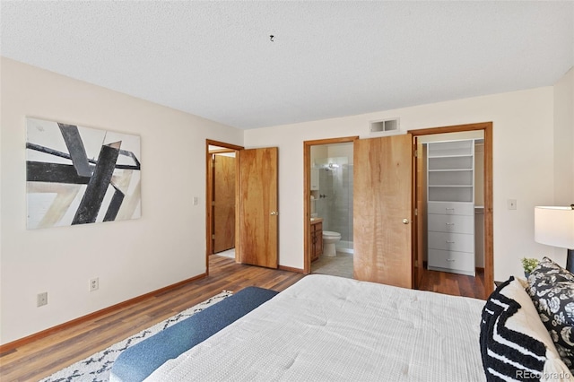 bedroom with a walk in closet, visible vents, ensuite bathroom, wood finished floors, and baseboards