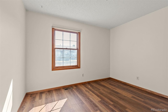 unfurnished room featuring visible vents, dark wood finished floors, a textured ceiling, and baseboards