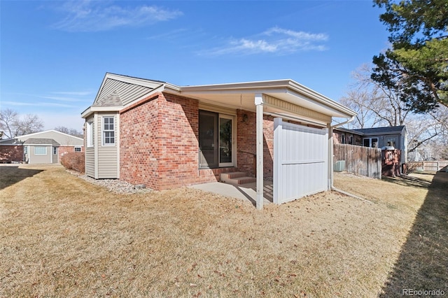 view of property exterior with brick siding, a lawn, and fence