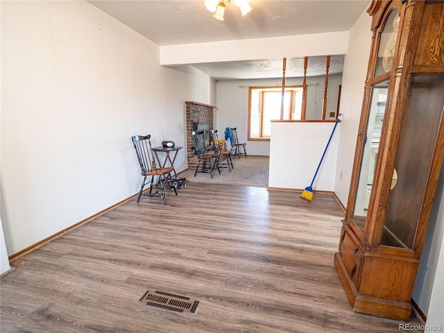 living area featuring visible vents, baseboards, a brick fireplace, and wood finished floors