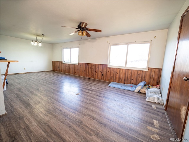 empty room featuring wainscoting, ceiling fan with notable chandelier, wood walls, and wood finished floors