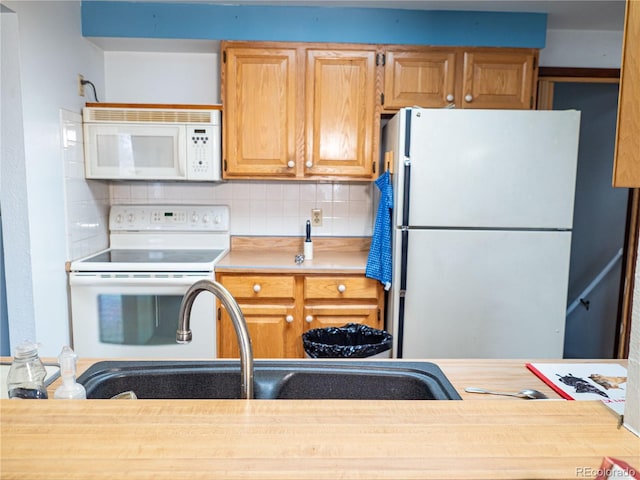 kitchen featuring decorative backsplash, white appliances, light countertops, and a sink