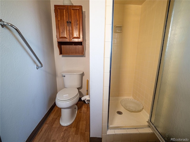 full bath featuring toilet, a stall shower, wood finished floors, baseboards, and a textured wall