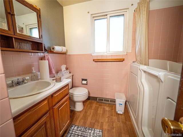 bathroom featuring toilet, vanity, wainscoting, wood finished floors, and tile walls