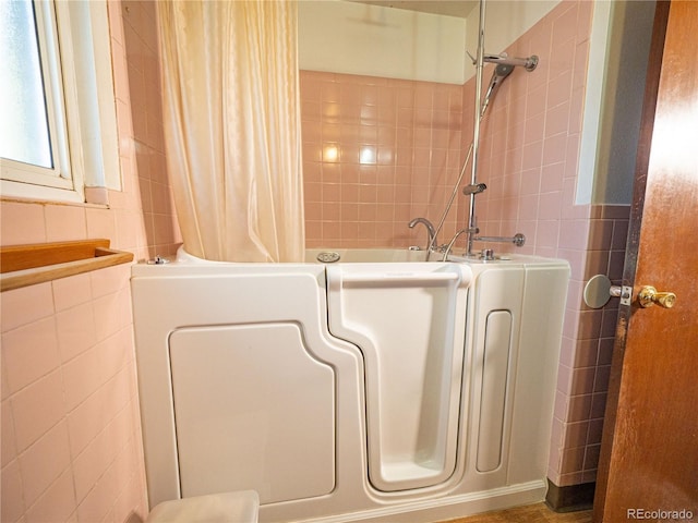 bathroom featuring curtained shower, a tub, and tile walls