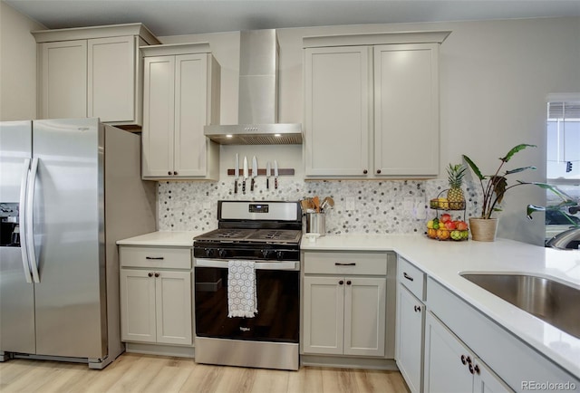 kitchen with light wood-style floors, appliances with stainless steel finishes, backsplash, wall chimney range hood, and a sink