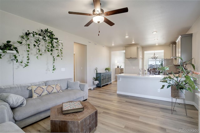 living area featuring light wood finished floors, recessed lighting, baseboards, and ceiling fan with notable chandelier