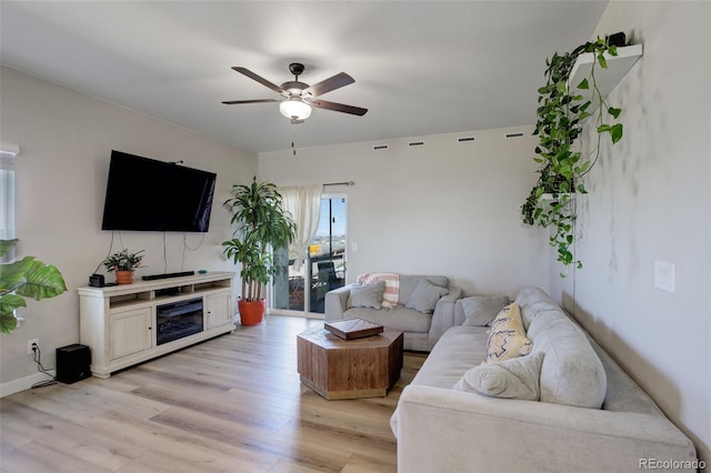 living area with a ceiling fan, baseboards, a fireplace, and light wood finished floors