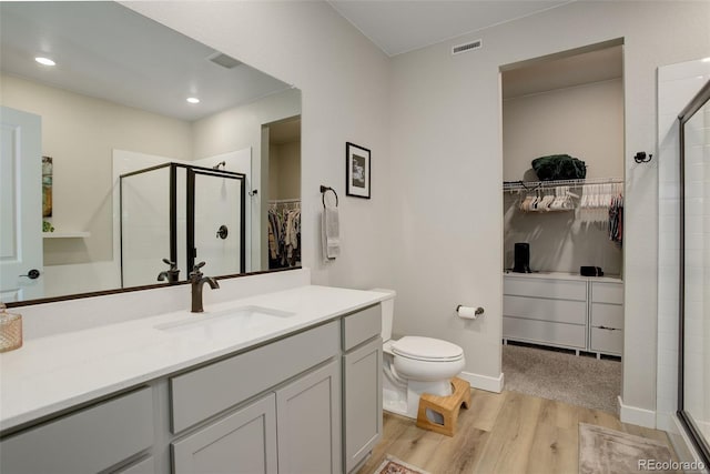 full bath with a stall shower, toilet, wood finished floors, a walk in closet, and vanity