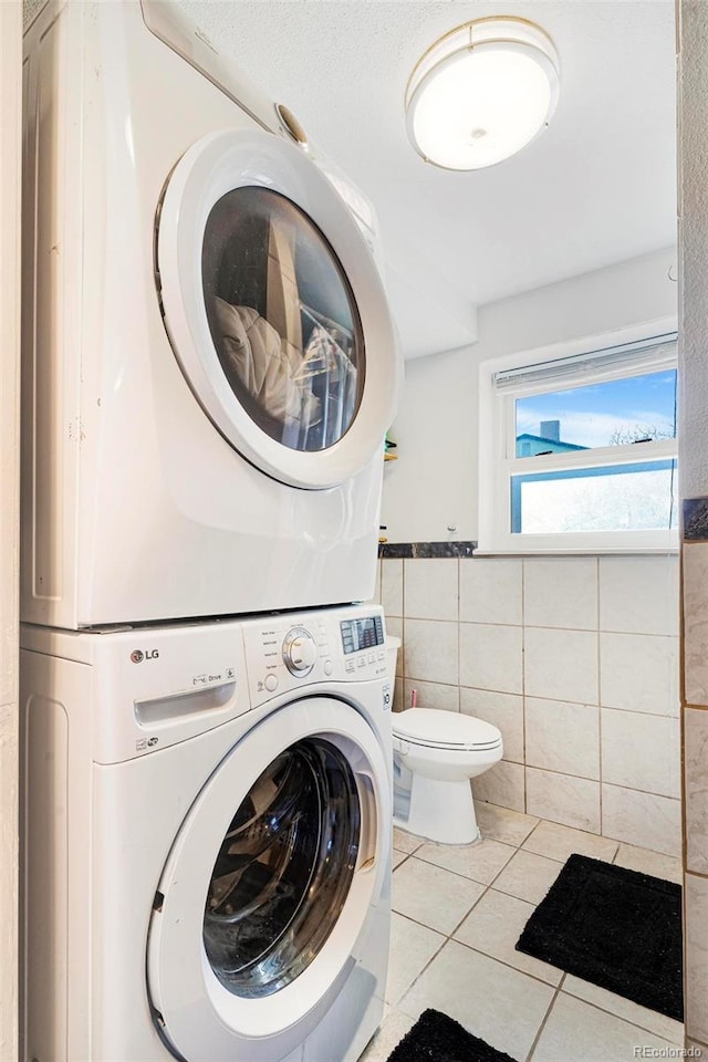 washroom featuring stacked washer / drying machine, tile walls, and light tile patterned flooring