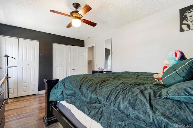 bedroom featuring a textured ceiling, wood-type flooring, ceiling fan, and two closets