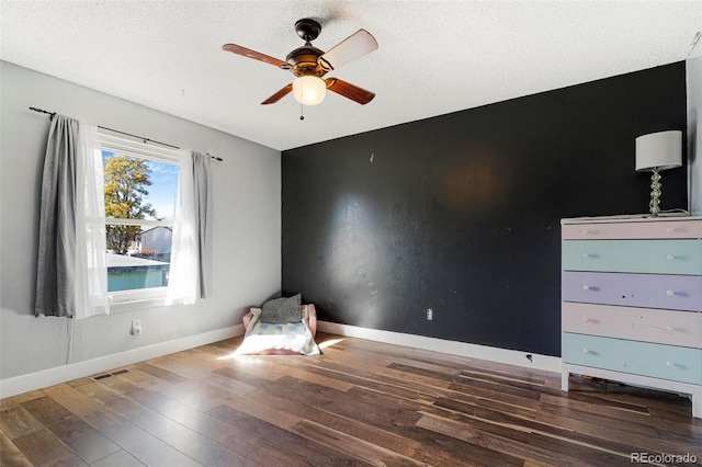 unfurnished bedroom with dark wood-type flooring, a textured ceiling, and ceiling fan