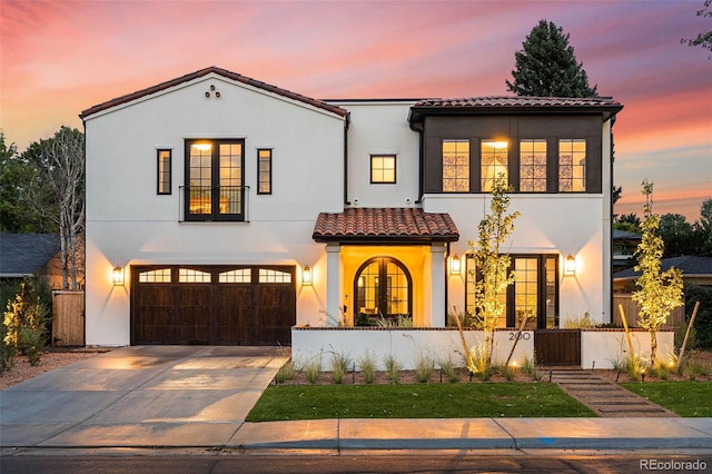mediterranean / spanish home featuring a tiled roof, a fenced front yard, stucco siding, a garage, and driveway