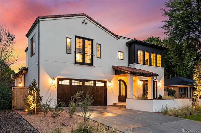 mediterranean / spanish house with driveway, a garage, stucco siding, fence, and a tile roof