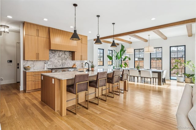 kitchen with a sink, decorative backsplash, light wood-style flooring, recessed lighting, and custom exhaust hood