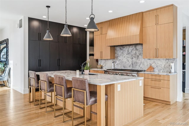 kitchen featuring custom exhaust hood, light wood finished floors, recessed lighting, tasteful backsplash, and light stone counters