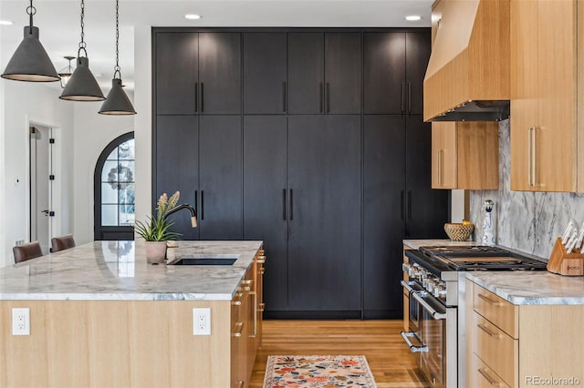 kitchen featuring high end stainless steel range oven, a sink, light wood-type flooring, a center island with sink, and light stone counters